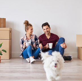 Couple sitting on floor, surrounded by moving boxes.