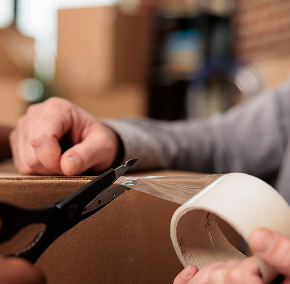 Person sealing a cardboard box with tape.